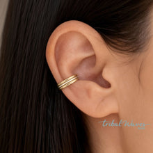 Load image into Gallery viewer, A close-up of a person's ear wearing a dainty gold and silver ear cuff with three parallel horizontal bands. Ear is surrounded by dark hair.