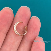 Load image into Gallery viewer, A close-up of a hand holding a slim, multi-band gold and silver ear cuff against a solid teal background.