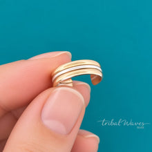 Load image into Gallery viewer, A close-up of a hand holding a slim, multi-band gold and silver ear cuff against a solid teal background.