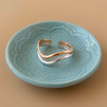 Load image into Gallery viewer, A double-band cuff ring with one polished wavy gold band and one polished wavy silver band, displayed on a light blue ceramic dish against a warm beige background.
