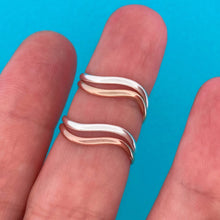 Load image into Gallery viewer, Two rings with wavy bands. One ring has a gold and silver band, while the other has a rose gold and silver band. Both worn on a person's fingers against a bright blue background.