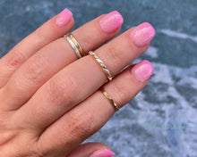Load image into Gallery viewer, Hand wearing three different rings as midi rings. Nails are long and pink over a blue water background.